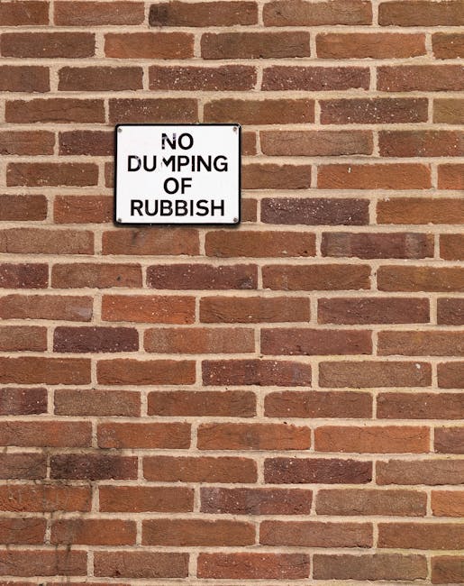 The image shows a collection of discarded household items and debris piled on a paved outdoor area next to a building wall. Prominently, there are multiple wooden ladders, some leaning against the wal